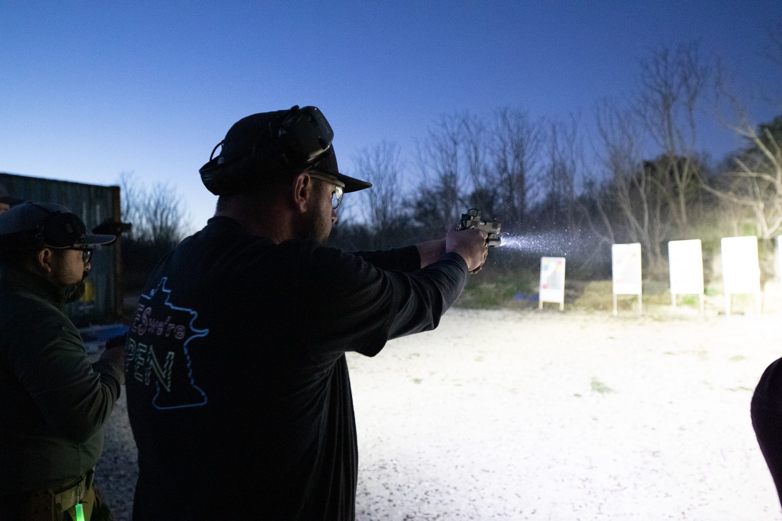 Combat Club member firing pistol with weapon-mounted light in low-light conditions