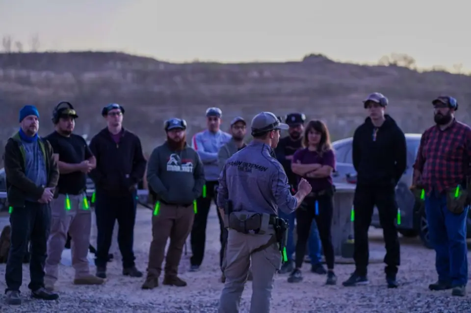 An instructor debriefing Combat Club members at dusk on the outdoor range